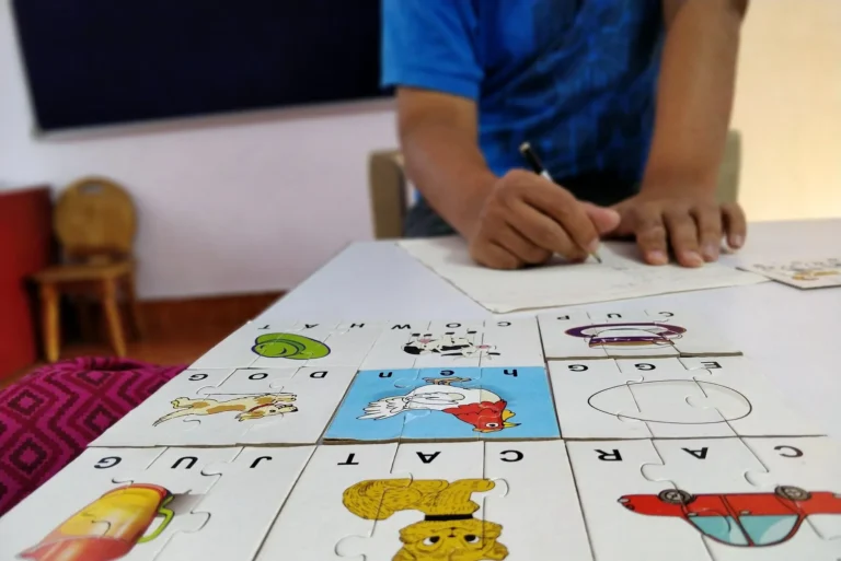 Picture-word puzzle pieces laid out on a table while a student writes with a pencil